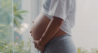 Close up of pregnant women gently holding her belly, wearing white t-shirt and gray sweat pants. 