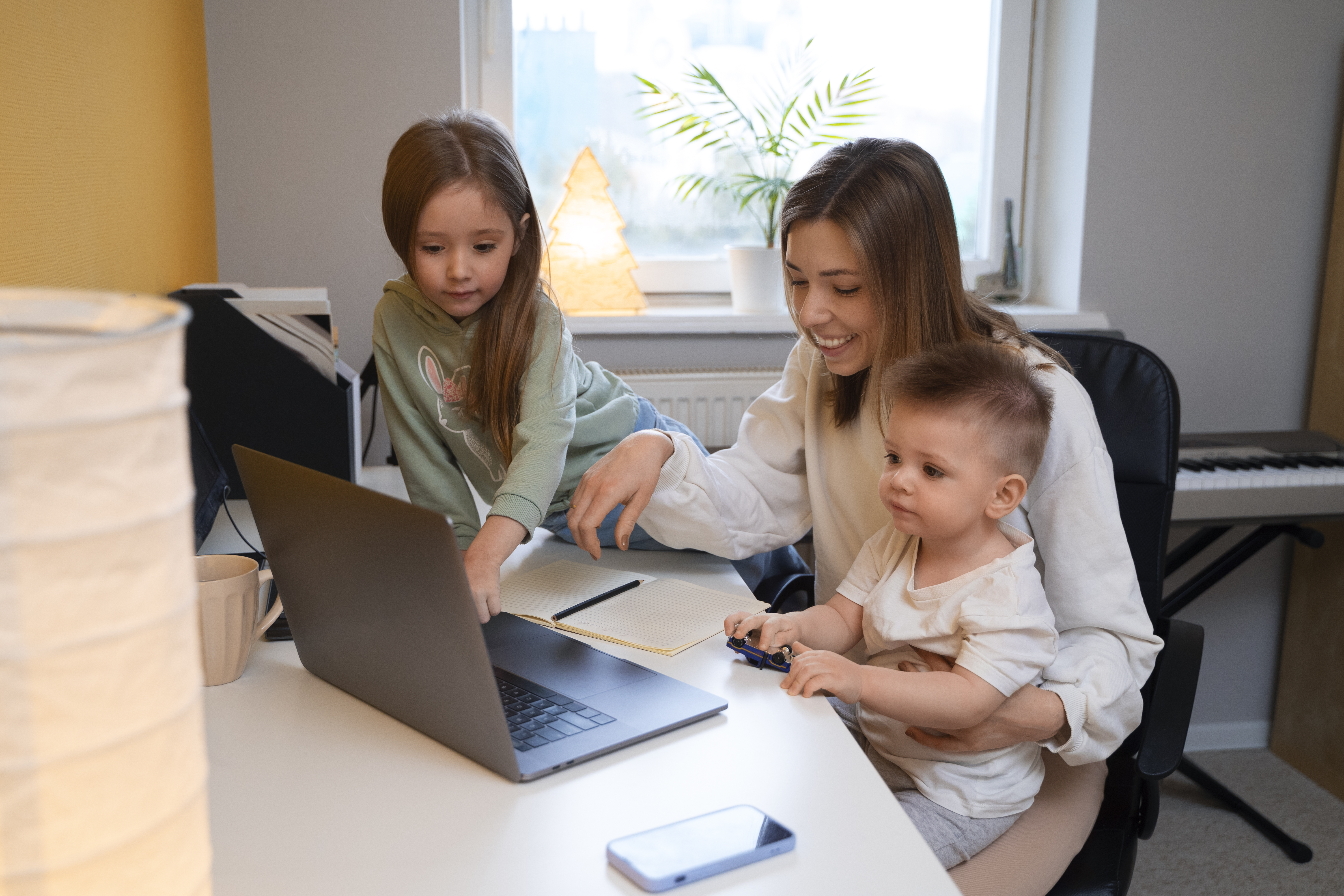 Little boy and little girl sitting with women in an at home office setting. Everyone is smiling 