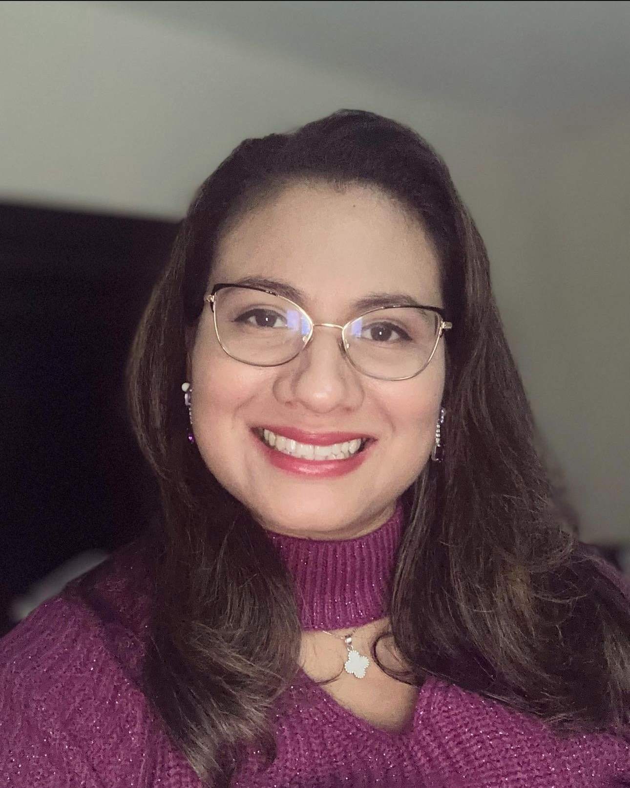 Adriana Morales Lemus, wearing purple sweater and glasses, smiles at camera. 