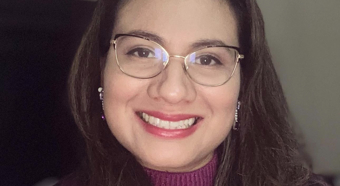 Adriana Morales Lemus, wearing purple sweater and glasses, smiles at camera. 