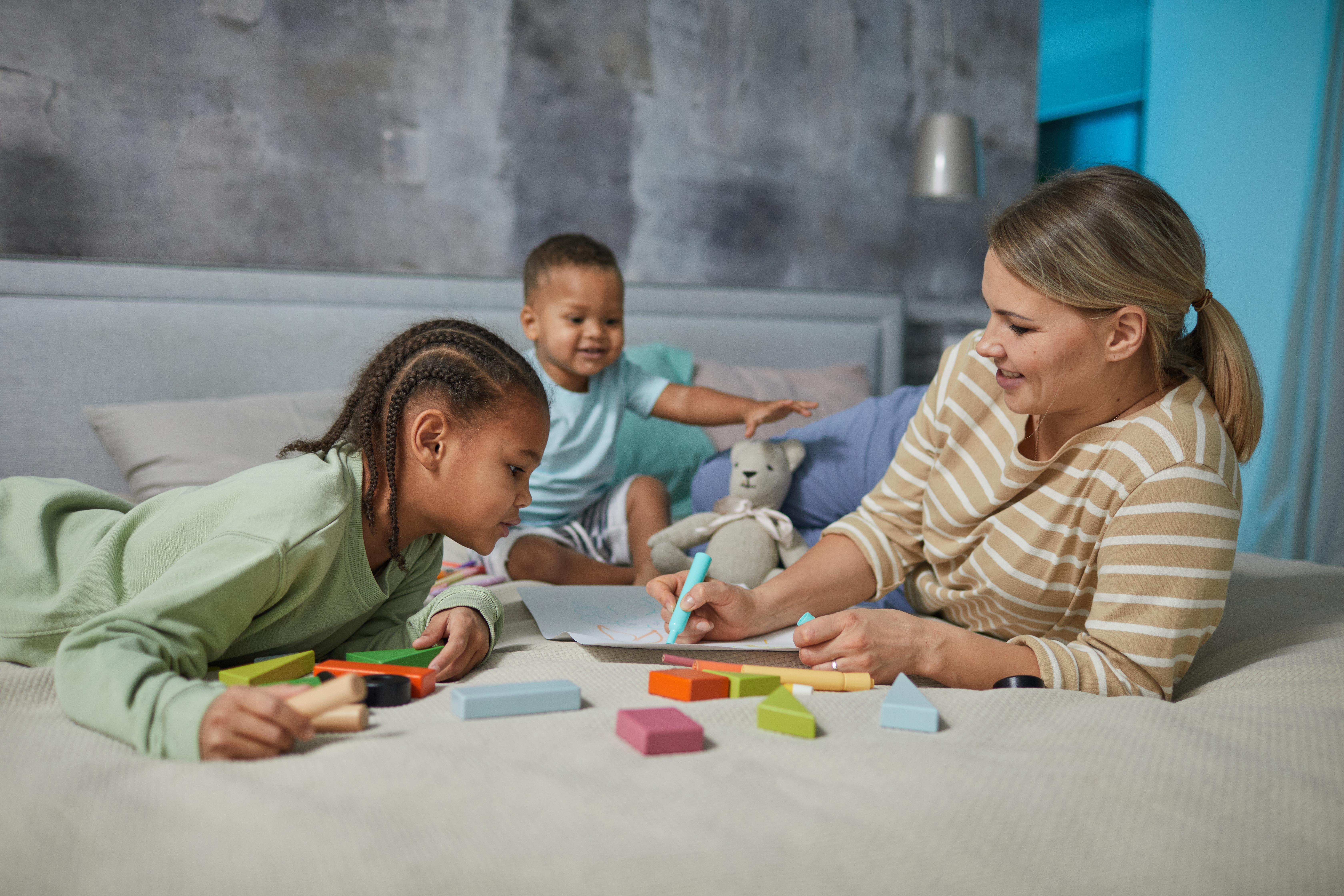 Women with two young kids in a at-home day care setting playing with toys 