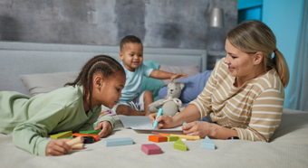 Women with two young kids in a at-home day care setting playing with toys 