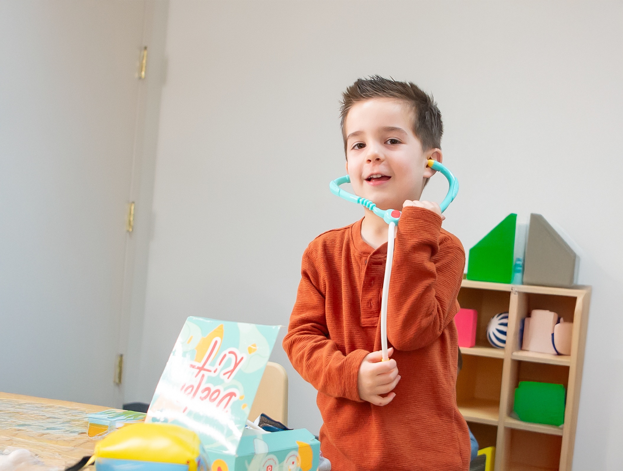 Young boy in orange shirt plays with toy stethoscope 