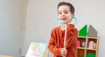 Young boy in orange shirt plays with toy stethoscope 