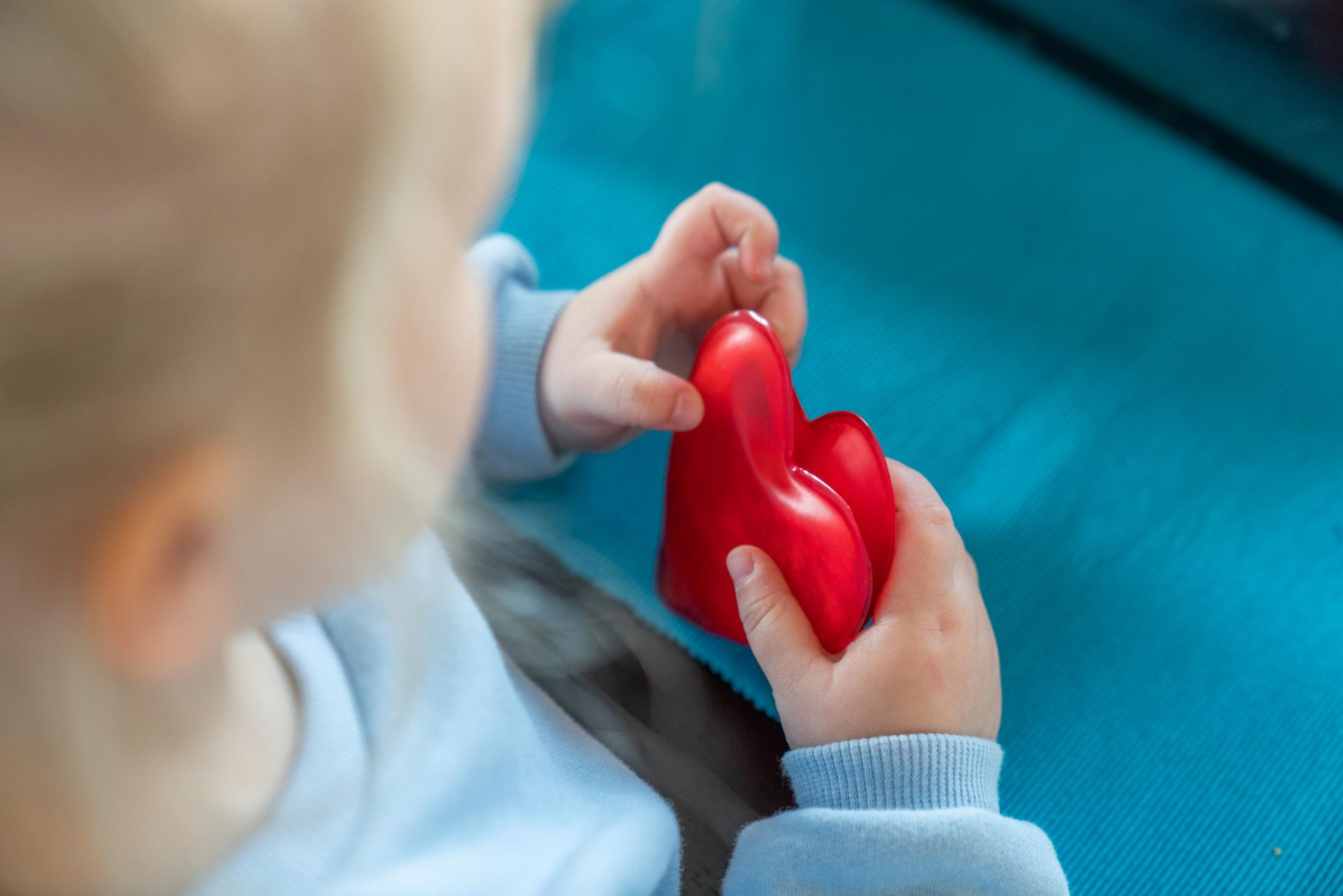 High angle photo of young girl looking down at a heart toy that she is holding in her hands, wearing baby blue sweater 