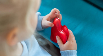 High angle photo of young girl looking down at a heart toy that she is holding in her hands, wearing baby blue sweater 