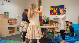 Group of 4 toddler girls play at a table with toys all over it. Laughing and smiling. 