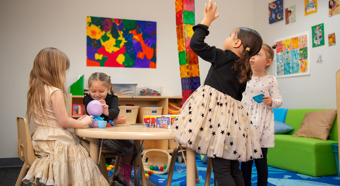 Four little girls in colorful classroom setting playing with toys