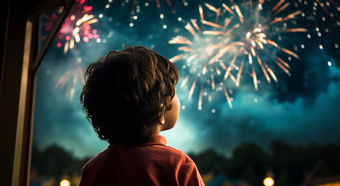 Young boy with brown shaggy hair and a red polo shirt stares out into the night sky with multiple color fireworks going off. 