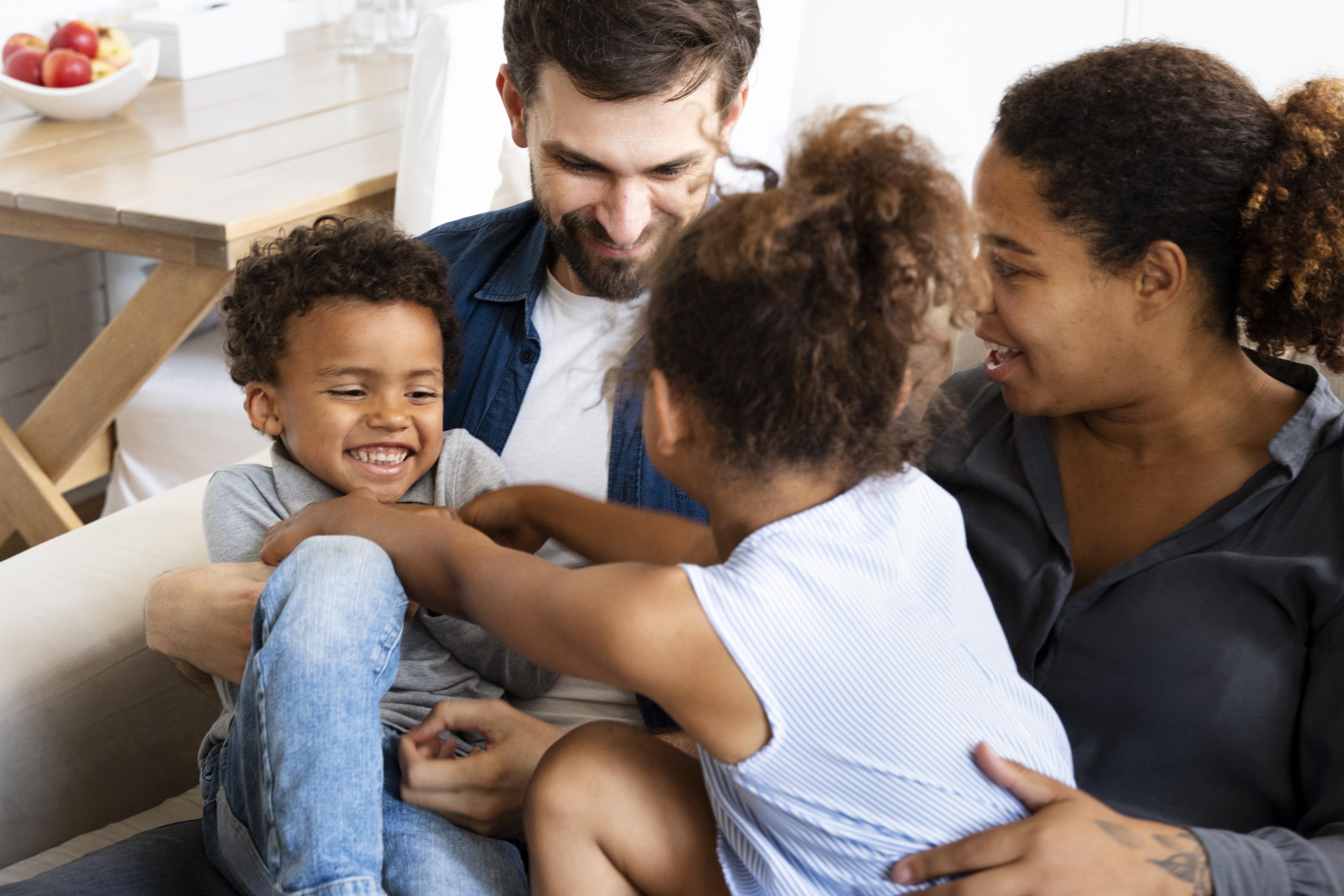 Two adults and two young children tickling each other on a couch.