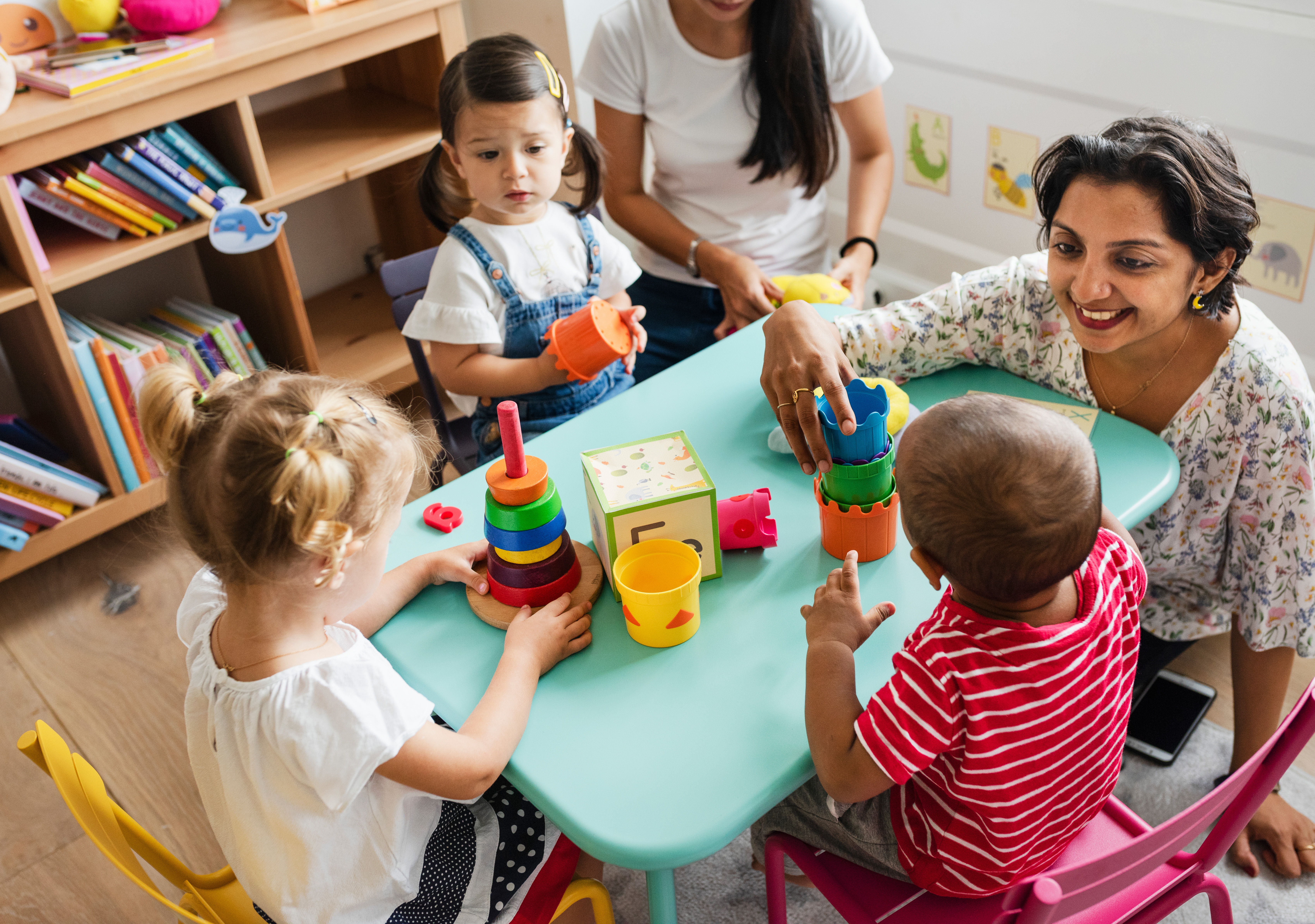 Three small children playing with toys with their teacher at a child sized table.