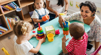 Three small children playing with toys with their teacher at a child sized table.