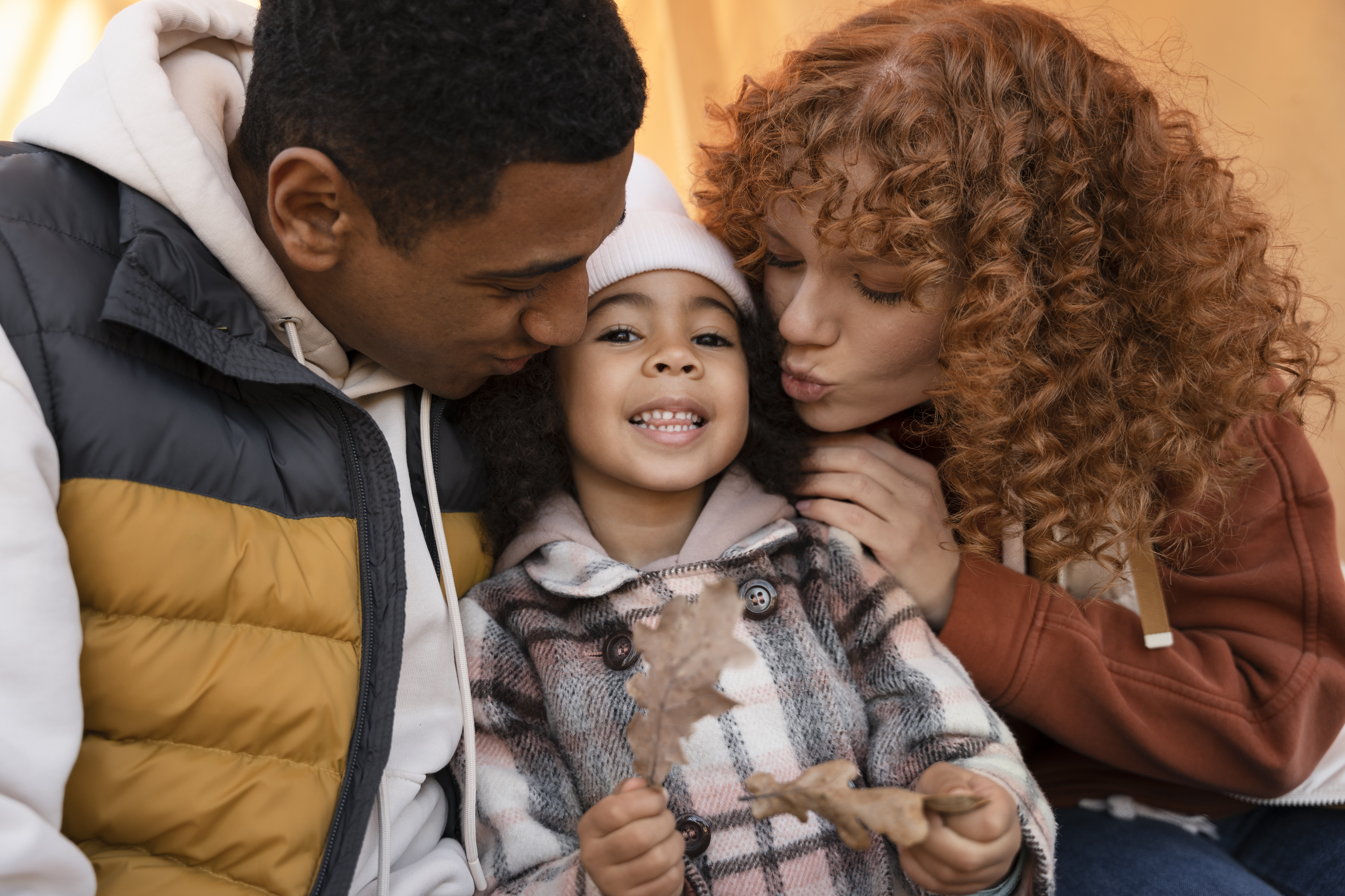 Young girl sitting in-between two young adults with warm weather clothing on