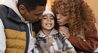 Young girl sitting in-between two young adults with warm weather clothing on