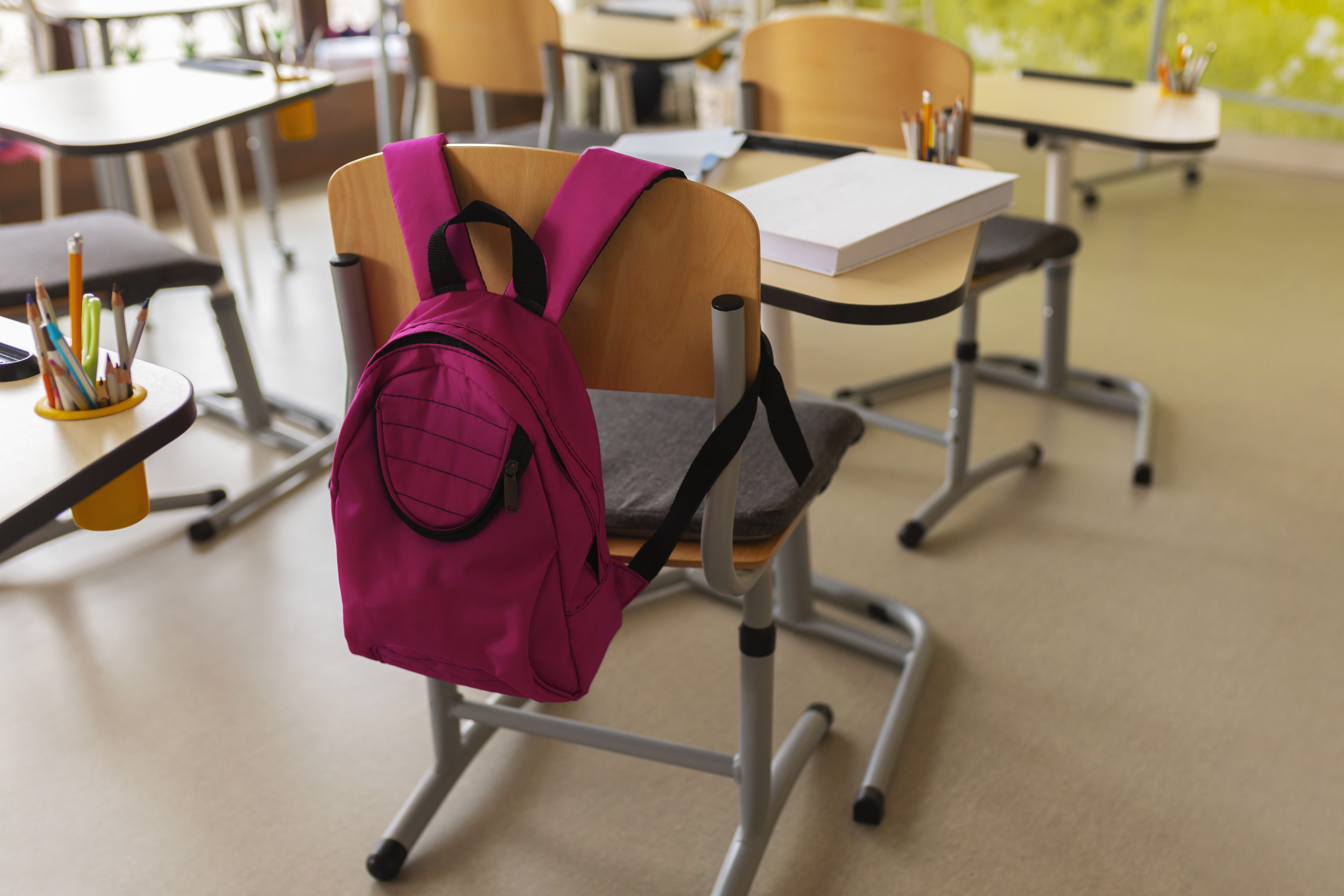 Interior of a classroom with a pink backpack on the back of the school desk chair.