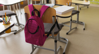 Interior of a classroom with a pink backpack on the back of the school desk chair.