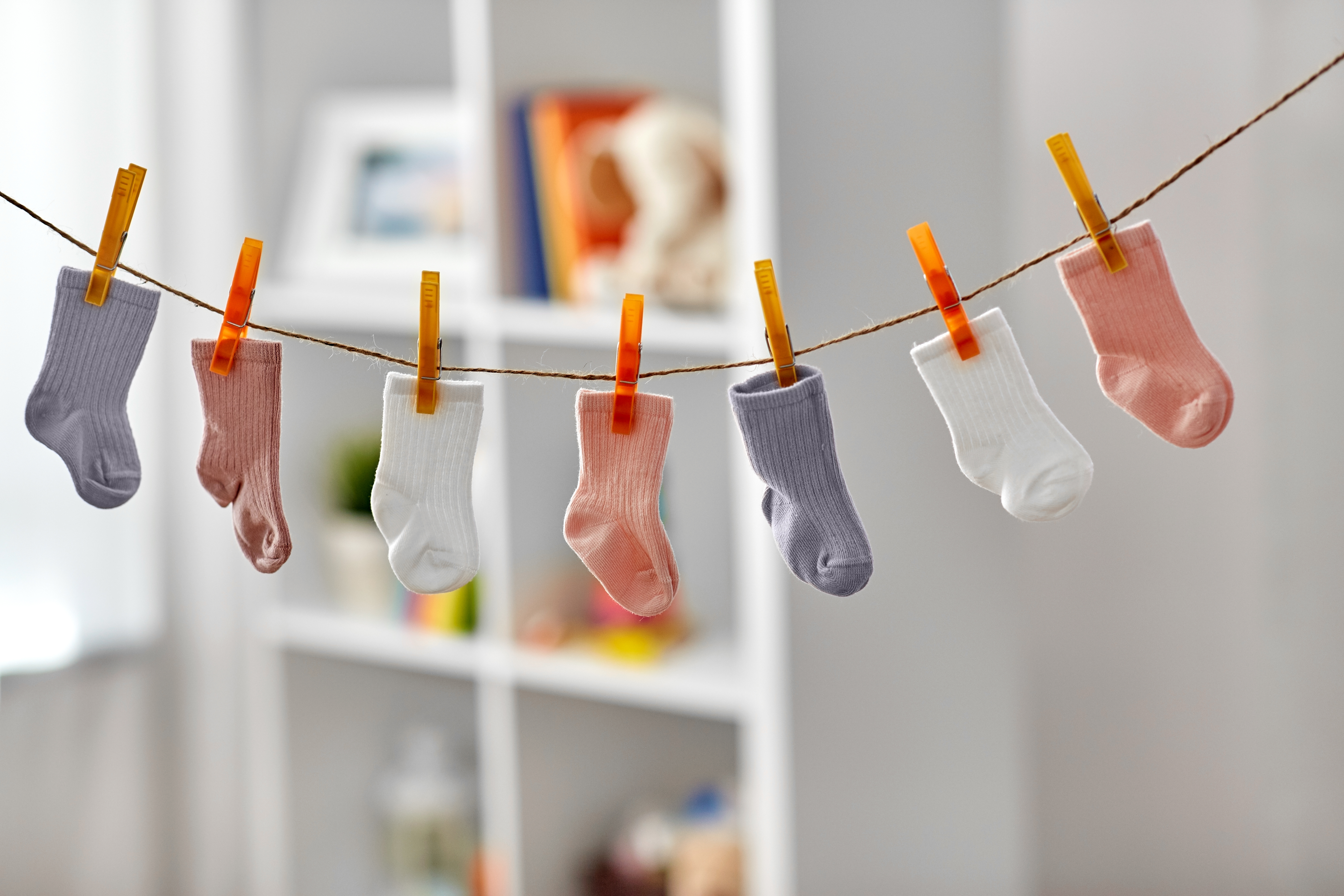 7 colored toddler sized socks hanging on a clothes line indoors.