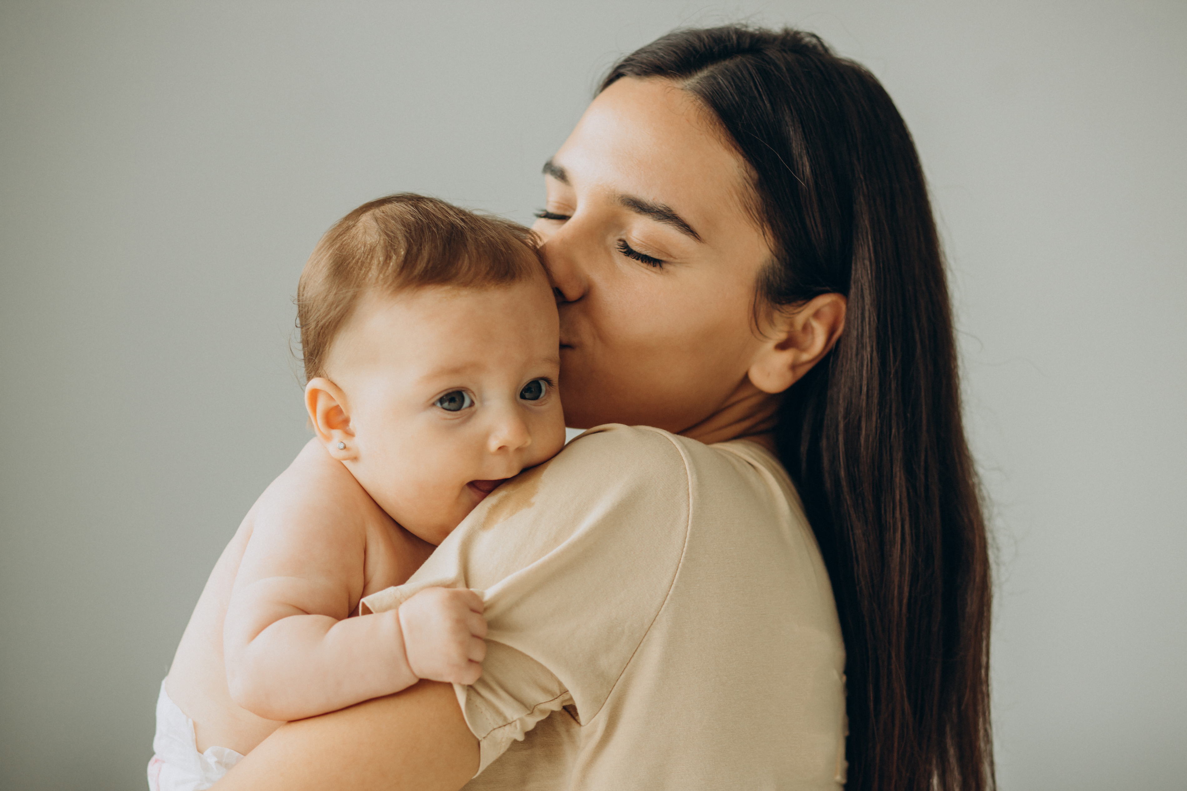 Brown haired women holding and kissing smiling baby on the head