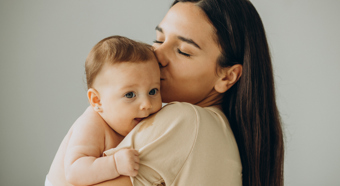 Brown haired women holding and kissing smiling baby on the head