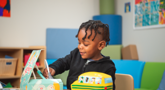 Young boy playing with toys while sitting at a desk in a fun classroom setting.