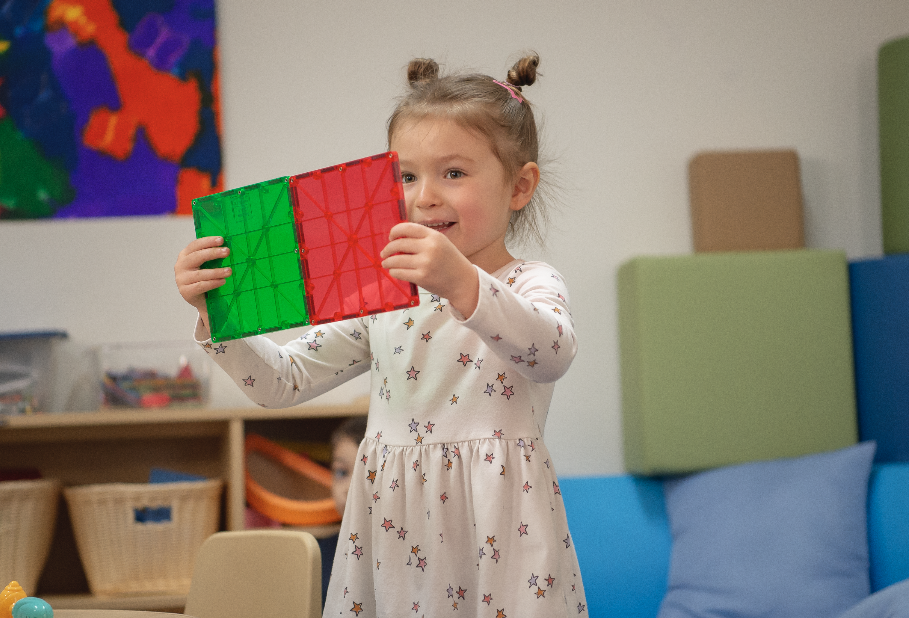 Young girl playing with red and green toy in a classroom setting.