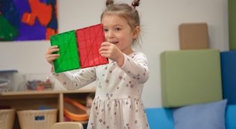 Young girl playing with red and green toy in a classroom setting.