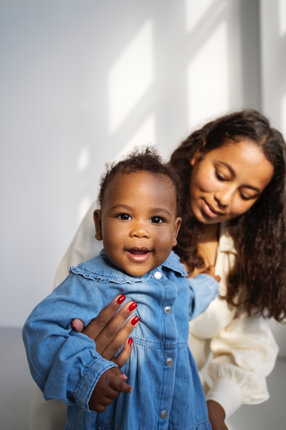 Women waring white dress holding young girl with a blue jean button up dress smiling into the camera