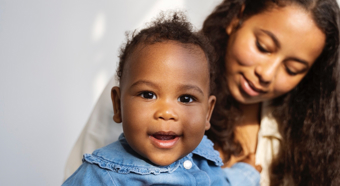 Women waring white dress holding young girl with a blue jean button up dress smiling into the camera