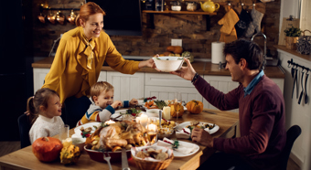 Thanksgiving dinner table with thanksgiving foods covering the table, young boy, girl, and two adults sitting around the table laughing and smiling