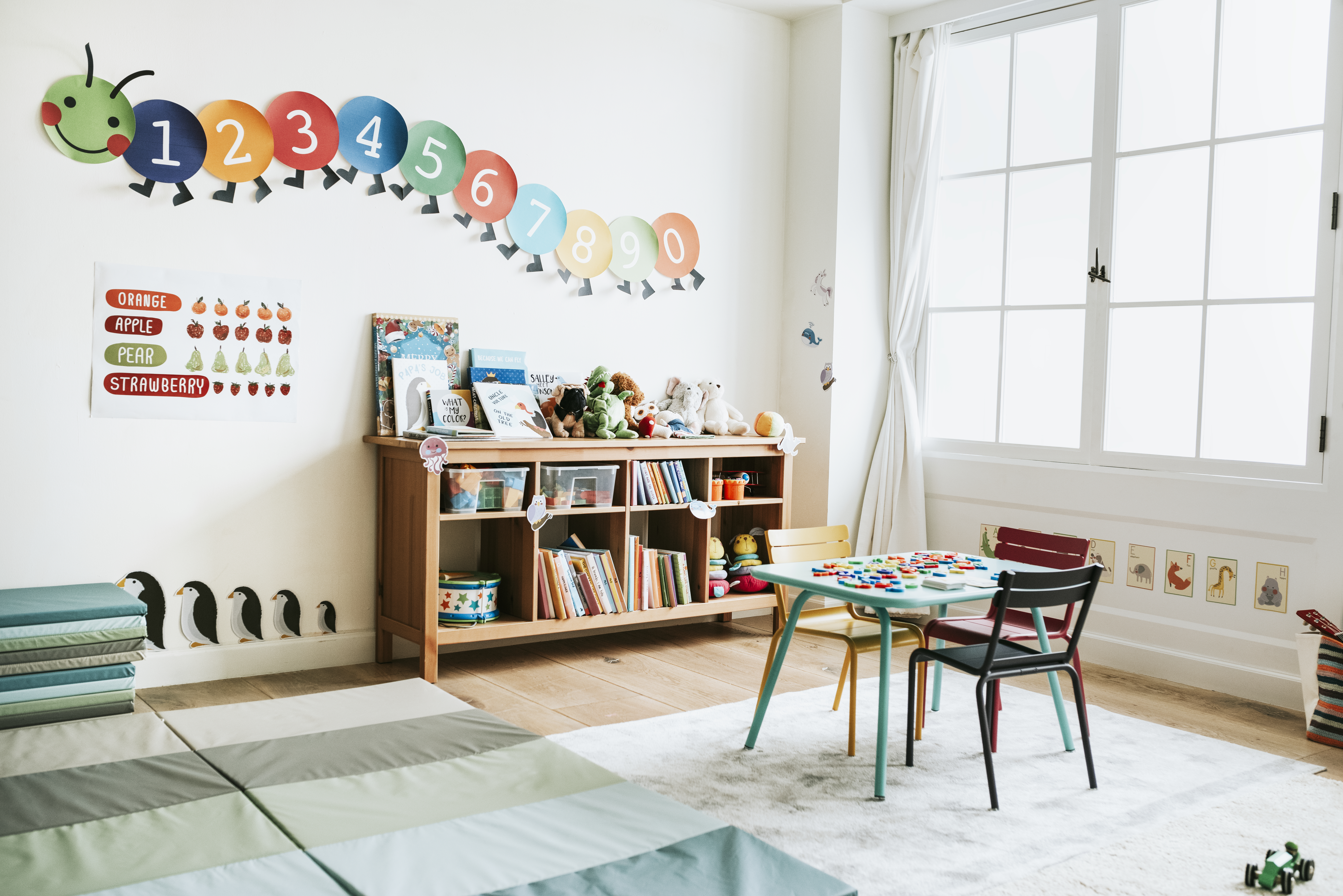 Preschool classroom interior with bookshelves, a little desk, and fun educational graphics on the walls. 