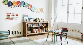 Preschool classroom interior with bookshelves, a little desk, and fun educational graphics on the walls. 