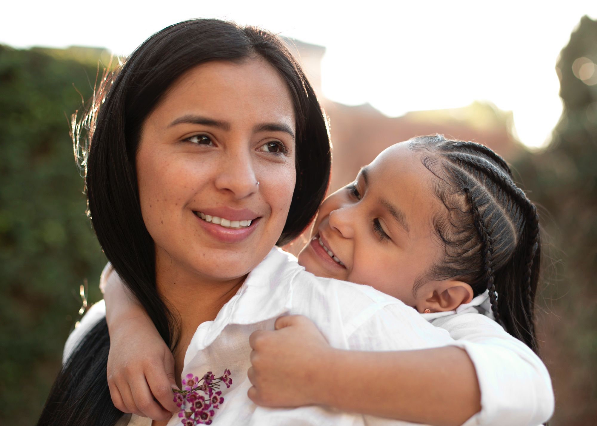 Women with smiling toddler on back wearing white shirts in an outdoor park setting 