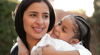 Women with smiling toddler on back wearing white shirts in an outdoor park setting 