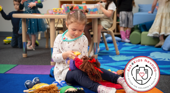 Little girl playing with dolls in a school setting with other kids 