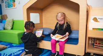Two small children sitting next to each other while reading children's books in a child's playhouse. 