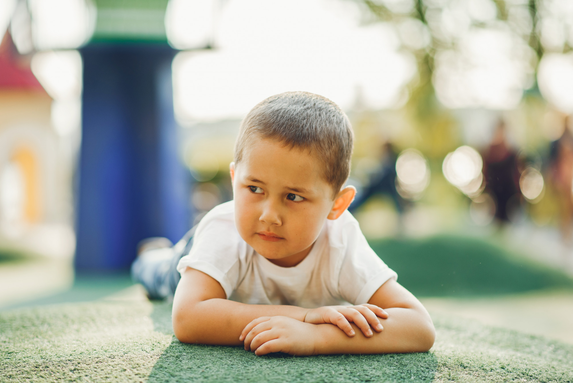 Baby boy lays on ground staring to the side, in an outdoor park setting 