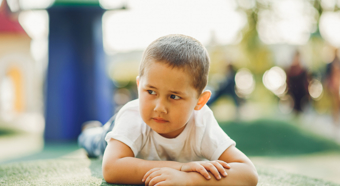 Baby boy lays on ground staring to the side, in an outdoor park setting 