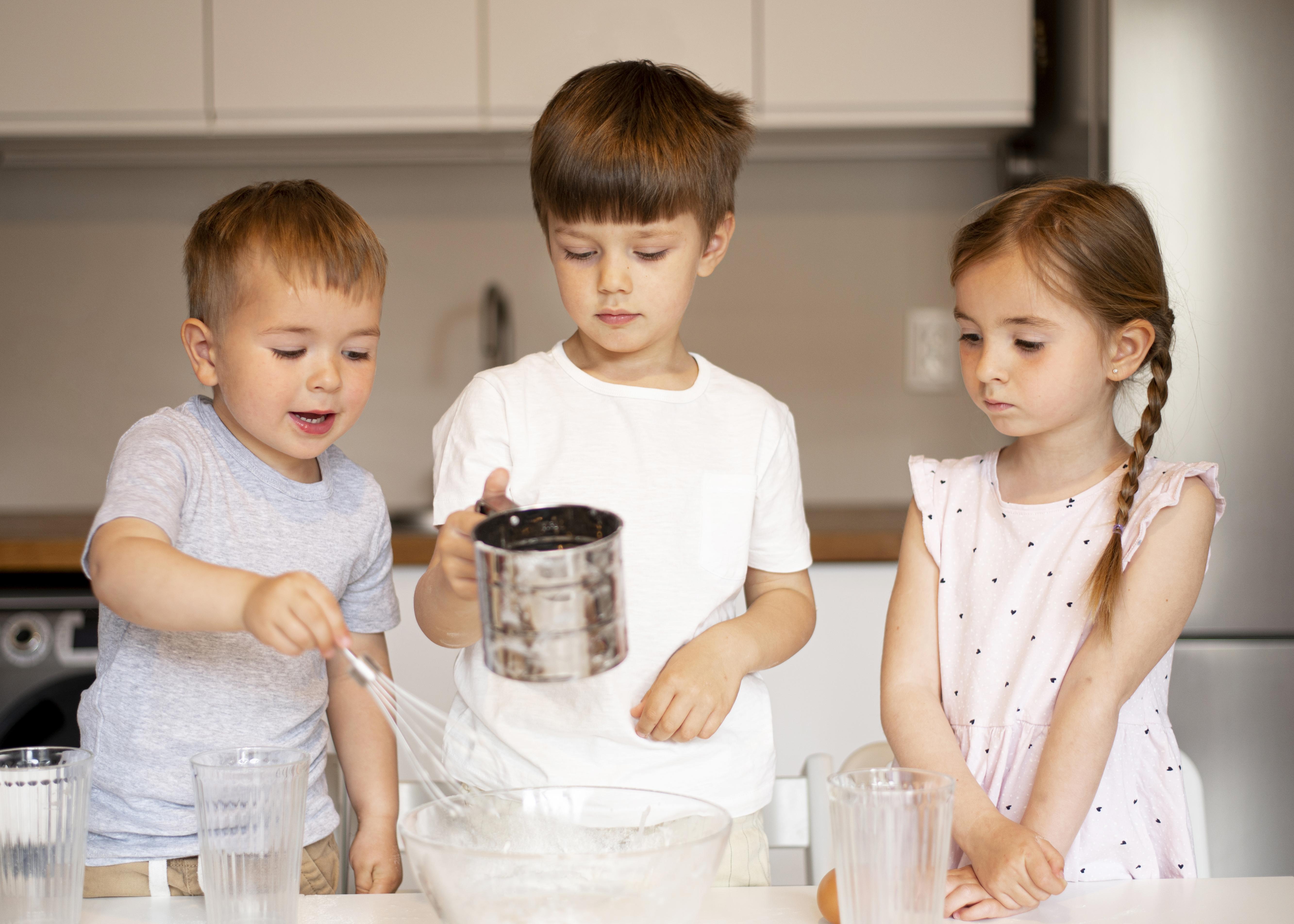 Three young kids in a home kitchen helping with some basic cooking.