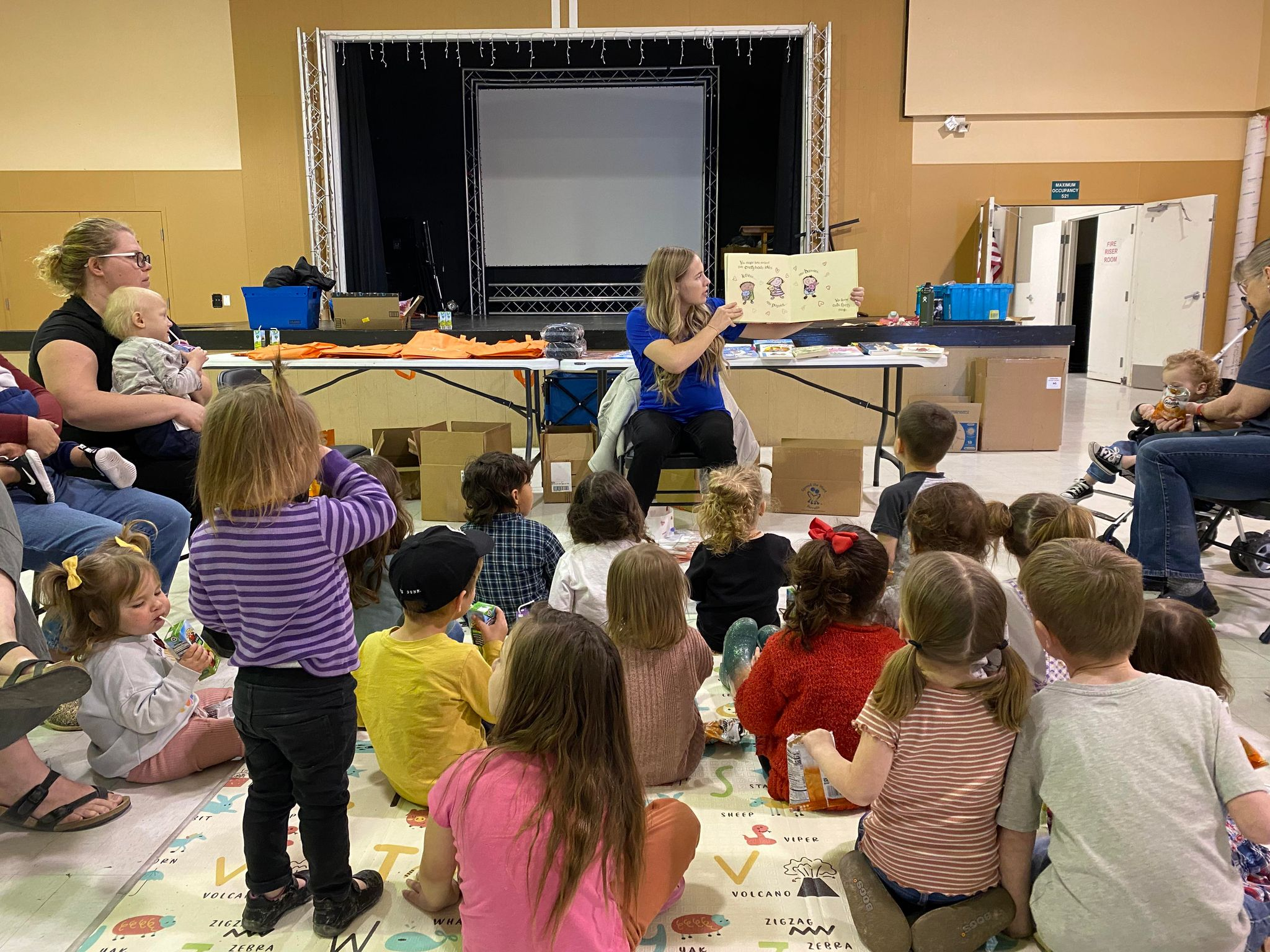 Children in a classroom being read a book by the teacher.