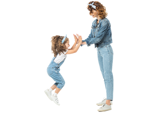 A light-skinned woman giving a double high five to a young girl who is jumping in the air. They are wearing matching blue jean outfits.