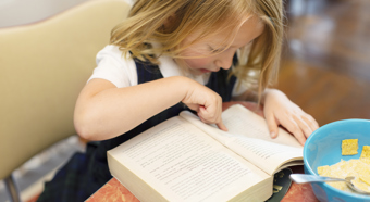 A little girl with blonde hair pointing her finger into a book, preparing for first day of school. 