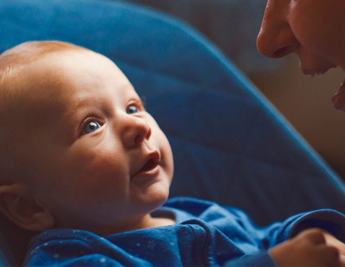 An infant with light skin and blue eyes is looking at an adult silhouette. 