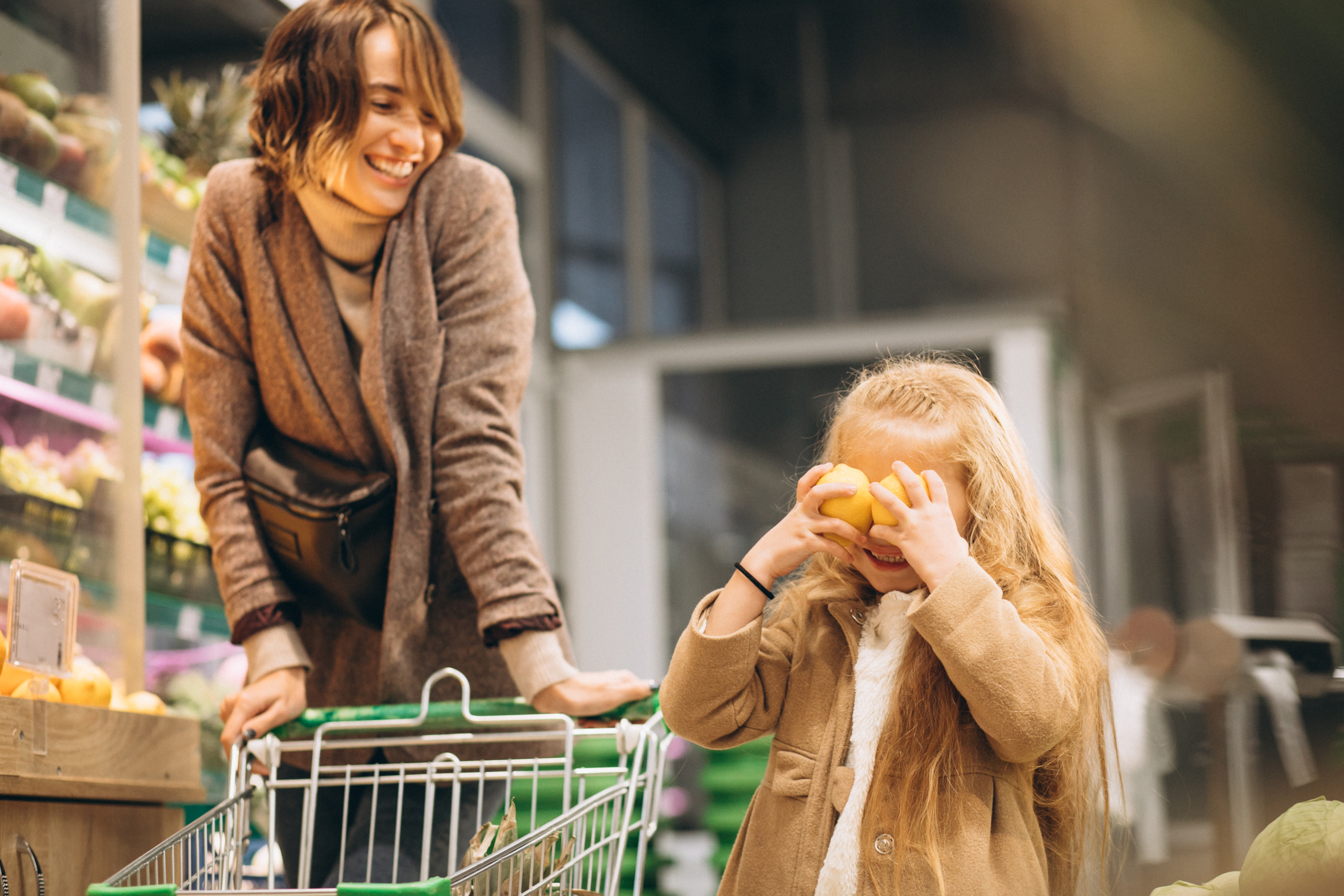 Adult female and young child push a child sized grocery cart through the store.