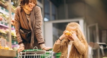 Adult female and young child push a child sized grocery cart through the store.