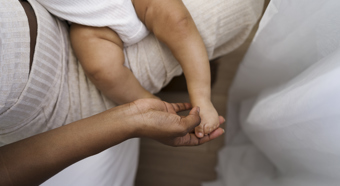 Overview angle of adult holding a little baby's foot while in her lap, all white clothing.