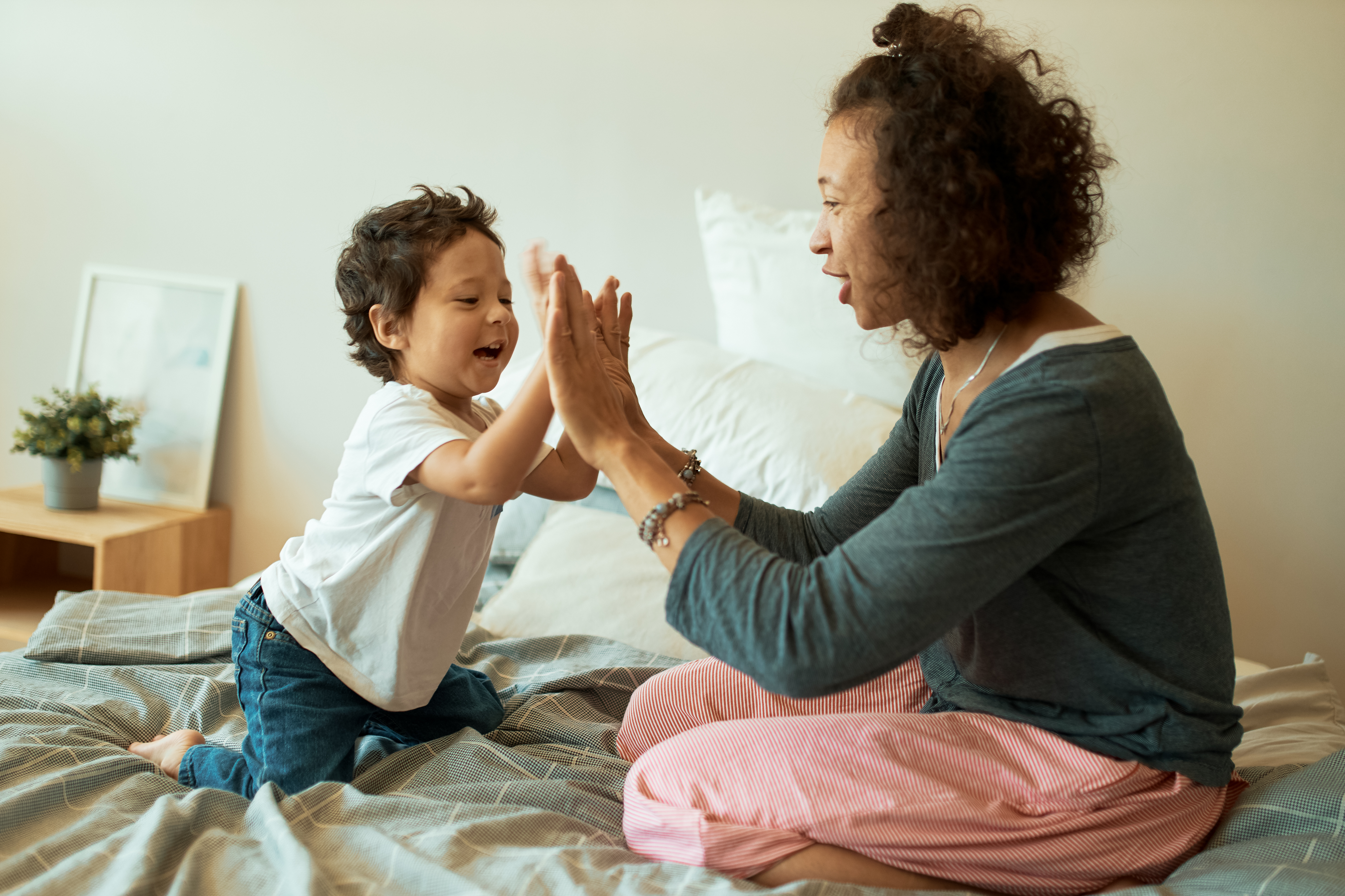 Happy women with a Baby Boy Playing Games at home Home, Cheerful Latin Female Clasping Hands With Infant baby Sitting in bed.