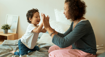 Happy women with a Baby Boy Playing Games at home Home, Cheerful Latin Female Clasping Hands With Infant baby Sitting in bed.