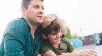 Adult male with young boy in outdoor setting. Both are looking off into the distance, smiling.