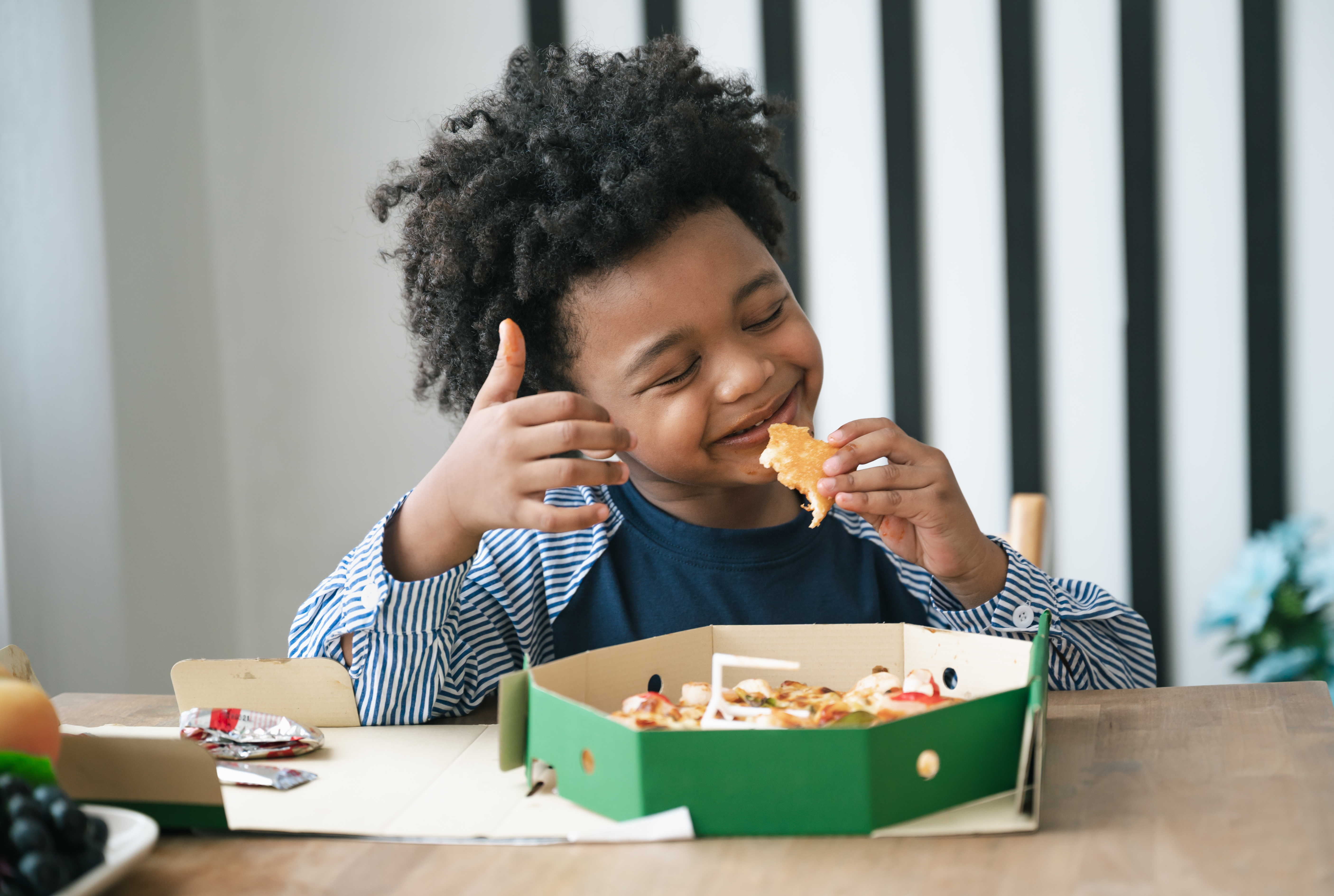 Young boy eating at a table with a big smile on his face. 