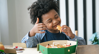 Young boy eating at a table with a big smile on his face. 